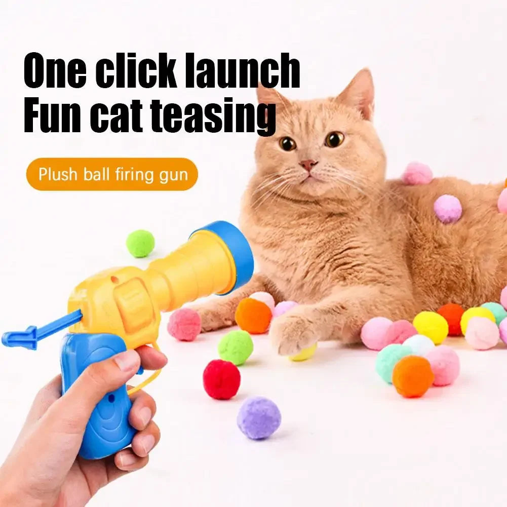 A cat is playing with a yellow plush ball firing gun and colorful soft balls on a white surface.