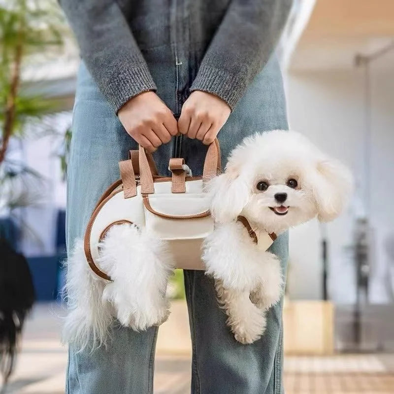 A small white poodle is being held in a breathable dog sling carrier by a person wearing blue jeans.
