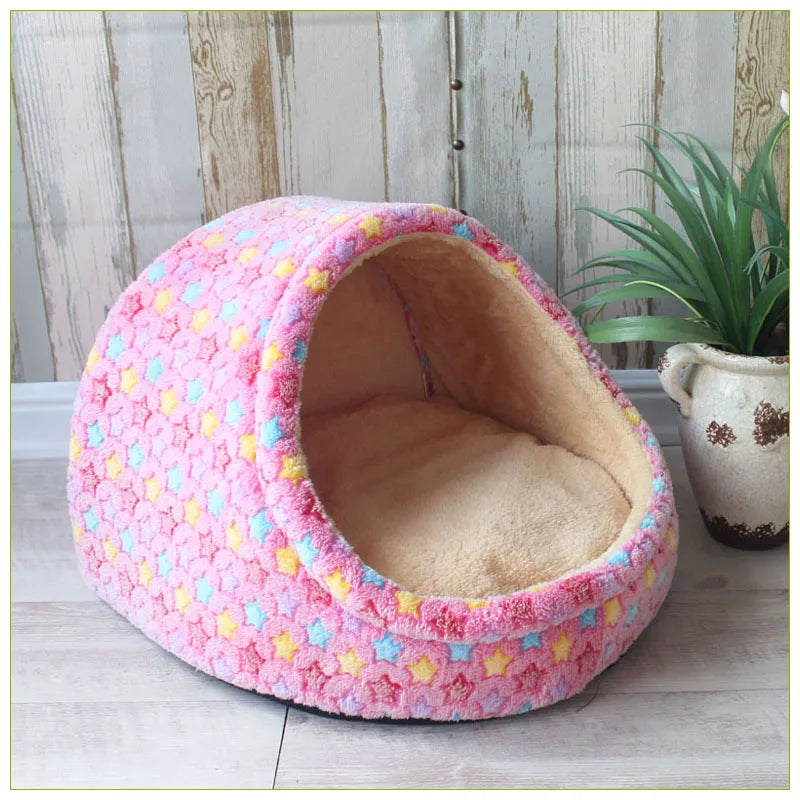 A pink, hexagonal pet bed shaped like a cave with a fuzzy interior, resting on a light wooden surface.