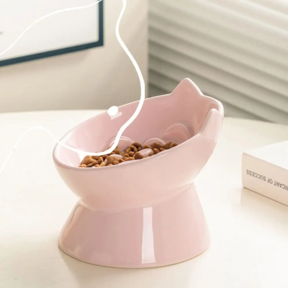 A pink ceramic pet food bowl with a raised slanted design sits on a white surface.