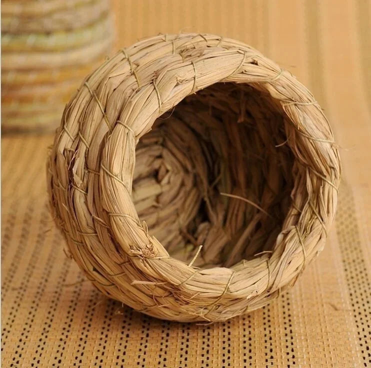 Nid pour oiseaux en paille naturelle tissée avec une ouverture circulaire, posé sur un tapis en osier.