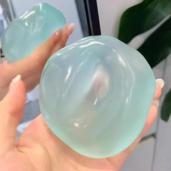 A hand holds a translucent pale blue silicone stress ball fidget toy with smooth, rounded surfaces.
