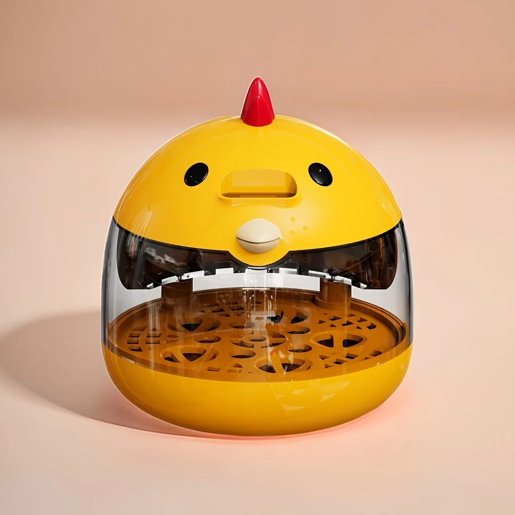 A yellow home egg incubator with a clear dome and a red comb, resting on a light pink surface.