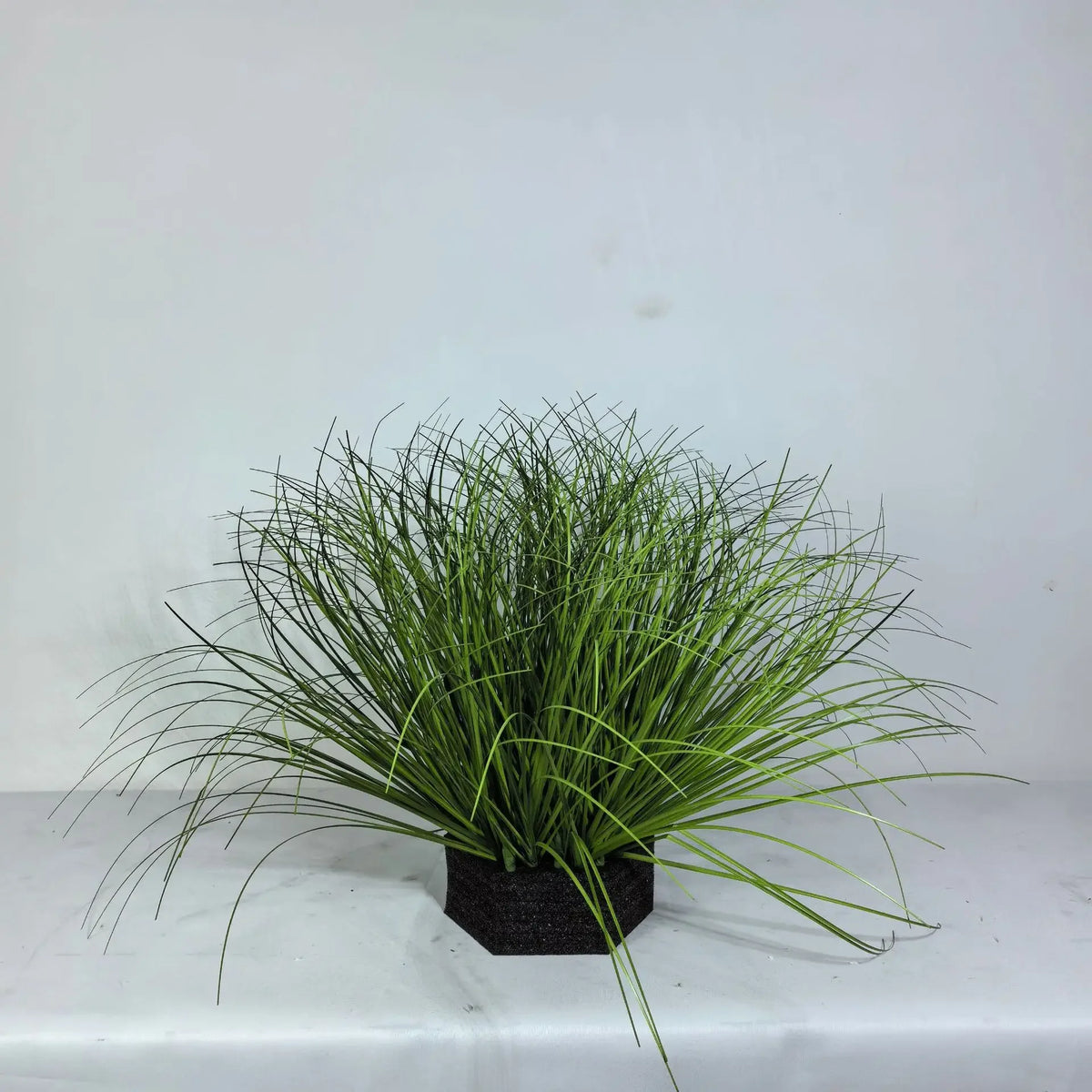 A clump of faux grass bush featuring reeds and onion grass planted in a dark pot.