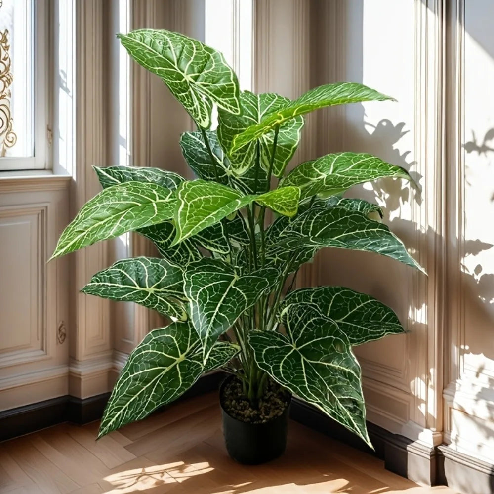 A large artificial Monstera plant with green leaves is displayed in a pot next to a window.