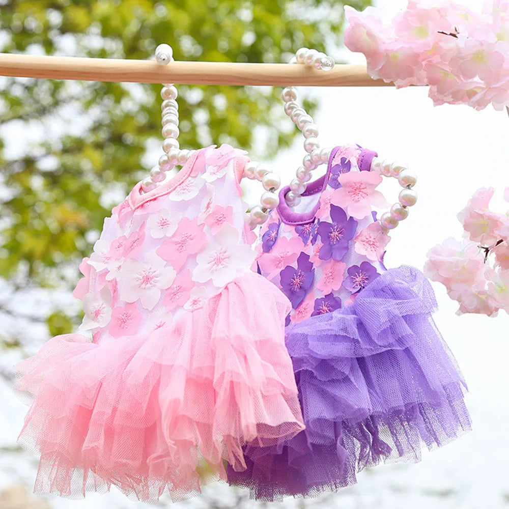 Robe en mousseline de dentelle florale rose et violette pour chien, suspendue à une barre en bois.