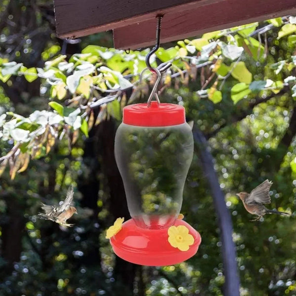 A clear glass bottle with an orange lid hangs from an iron hook, positioned among green leaves.