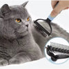 A hand is using a black stainless steel pet deshedding comb on a gray cat's fur.
