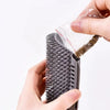 A hand is holding a black massage brush with a clear plastic bag containing hair.