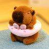Braune Capybara-Plüschpuppe mit pinkem Hoodie und Flügel, sitzt auf blauer Oberfläche.