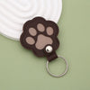 A brown leather paw print charm with a silver ring attached, resting on a light green surface.
