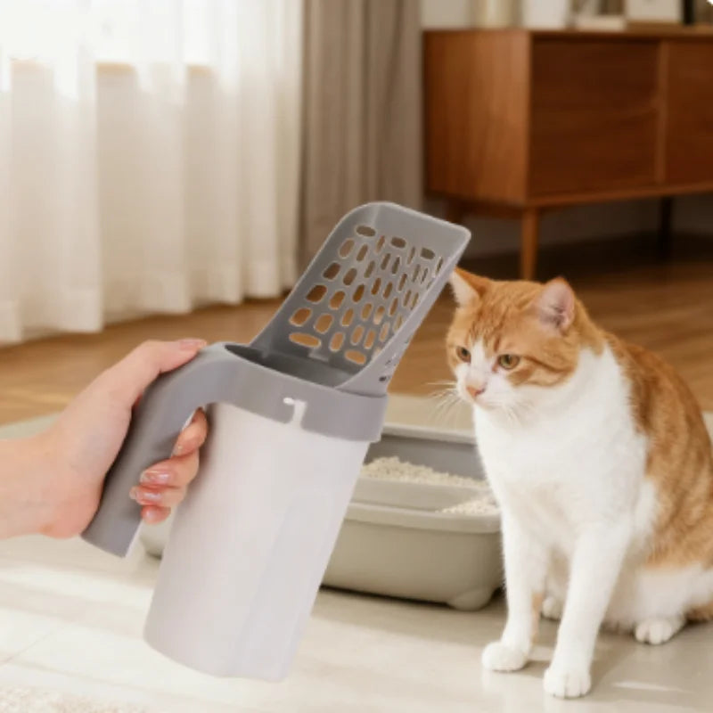 A hand is using a gray self-cleaning cat litter scoop with a filter to scoop litter from a tray.