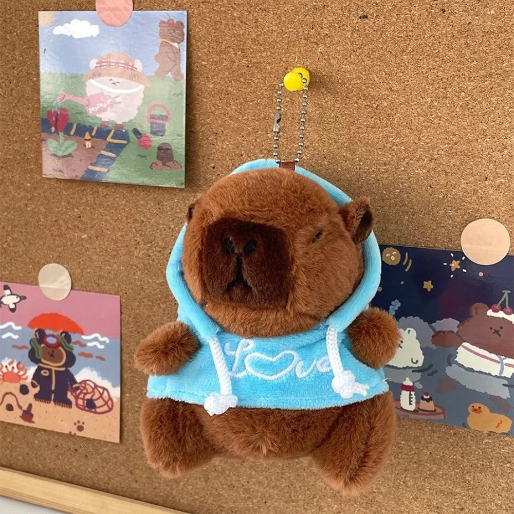 Braune Capybara-Plüsch-Hoodiepuppe mit hellblauer Stoff und weißem Zierrand auf einer Korkwand