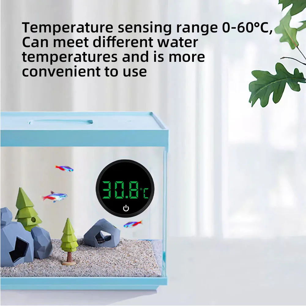 A blue digital aquarium thermometer is shown with a green plant and small decorative rocks inside, displaying a temperature o