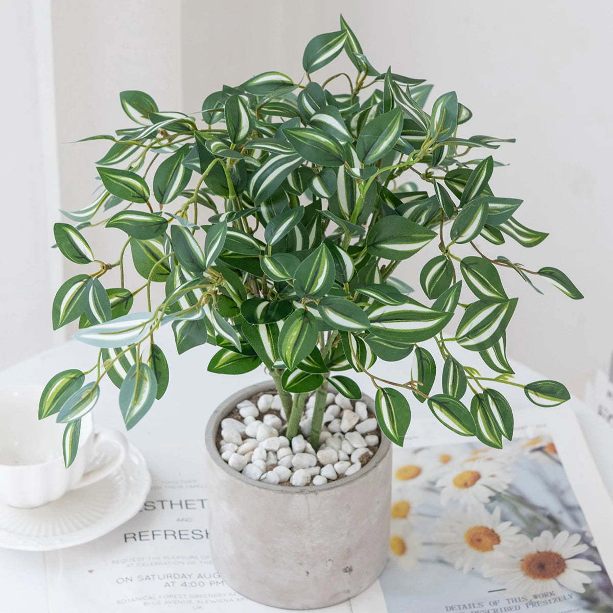 Artificial bonsai tree with green leaves in a pot displayed on a white surface.