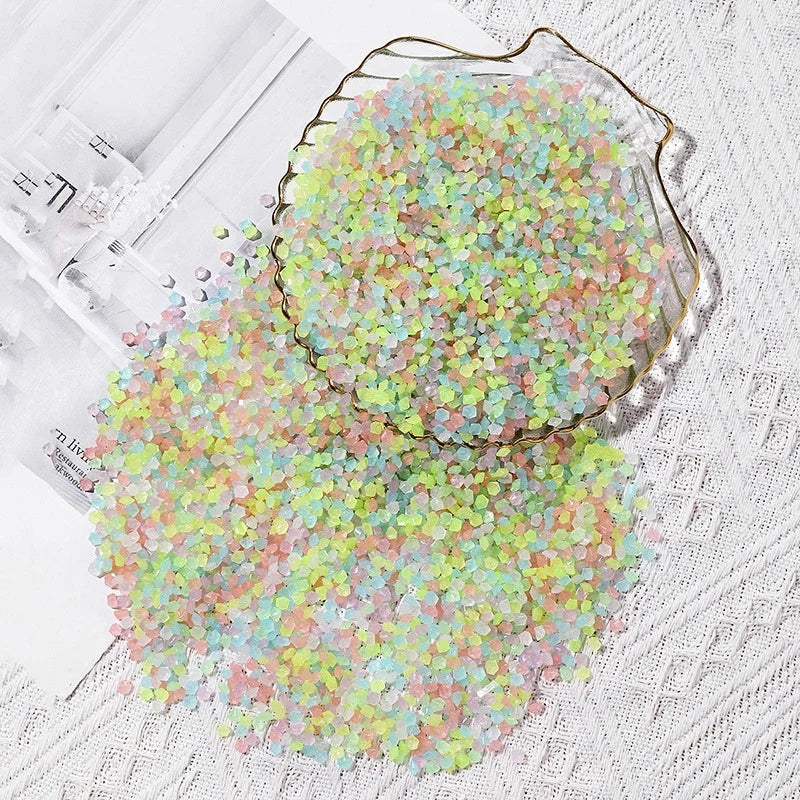 A pile of glow-in-the-dark decorative pebbles in shades of green and pink scattered on a white surface.