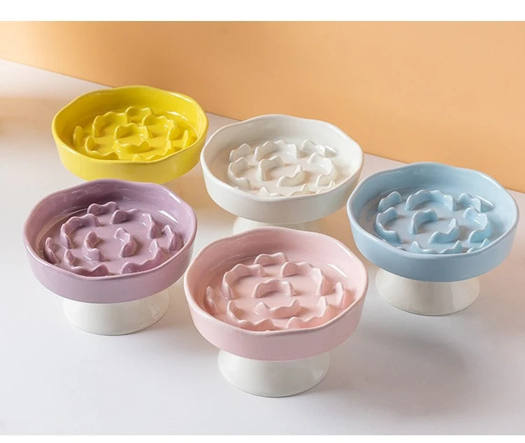 A set of ceramic elevated bowls in yellow, white, purple, and blue for pets.