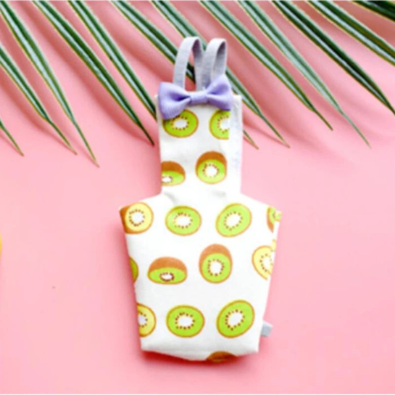 A white parrot-themed diaper with a purple bow tie and green fruit patterns, set against a pink background.