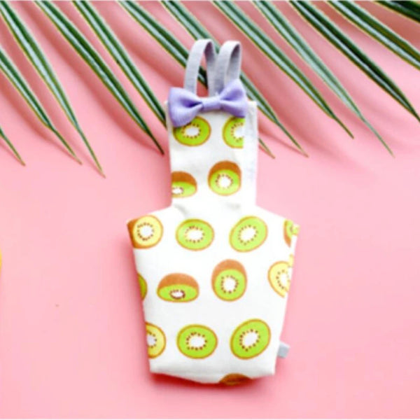 A white parrot-themed diaper with a purple bow tie and green fruit patterns, set against a pink background.