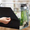 A hand is holding a black aquarium background film box over a glass aquarium with aquatic plants.