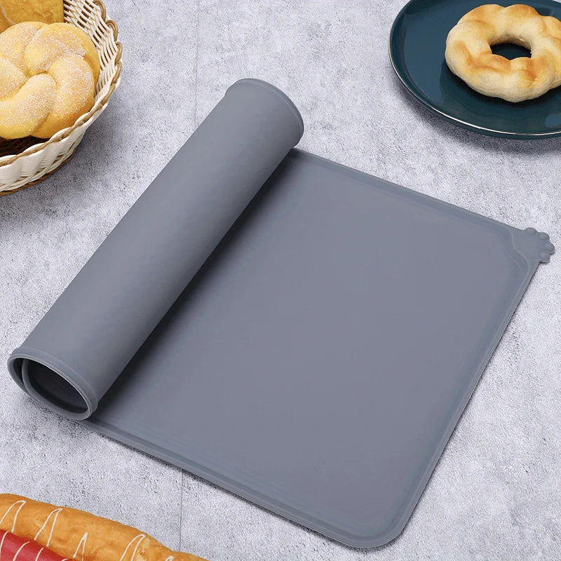 A gray silicone pet feeding mat with raised edges is shown next to baked goods on a light gray surface.