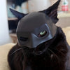 A black cat wearing a gray bat wing mask covering its face.