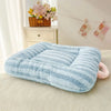 A light blue, striped plush oval pet bed for cats and small dogs resting on a cream-colored surface.