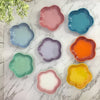 A collection of colorful, flower-shaped ceramic bowls and dishes in shades of pink, blue, green, orange, and purple arranged 