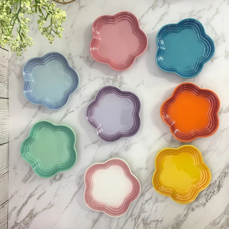 A collection of colorful, flower-shaped ceramic bowls and dishes in shades of pink, blue, green, orange, and purple arranged 