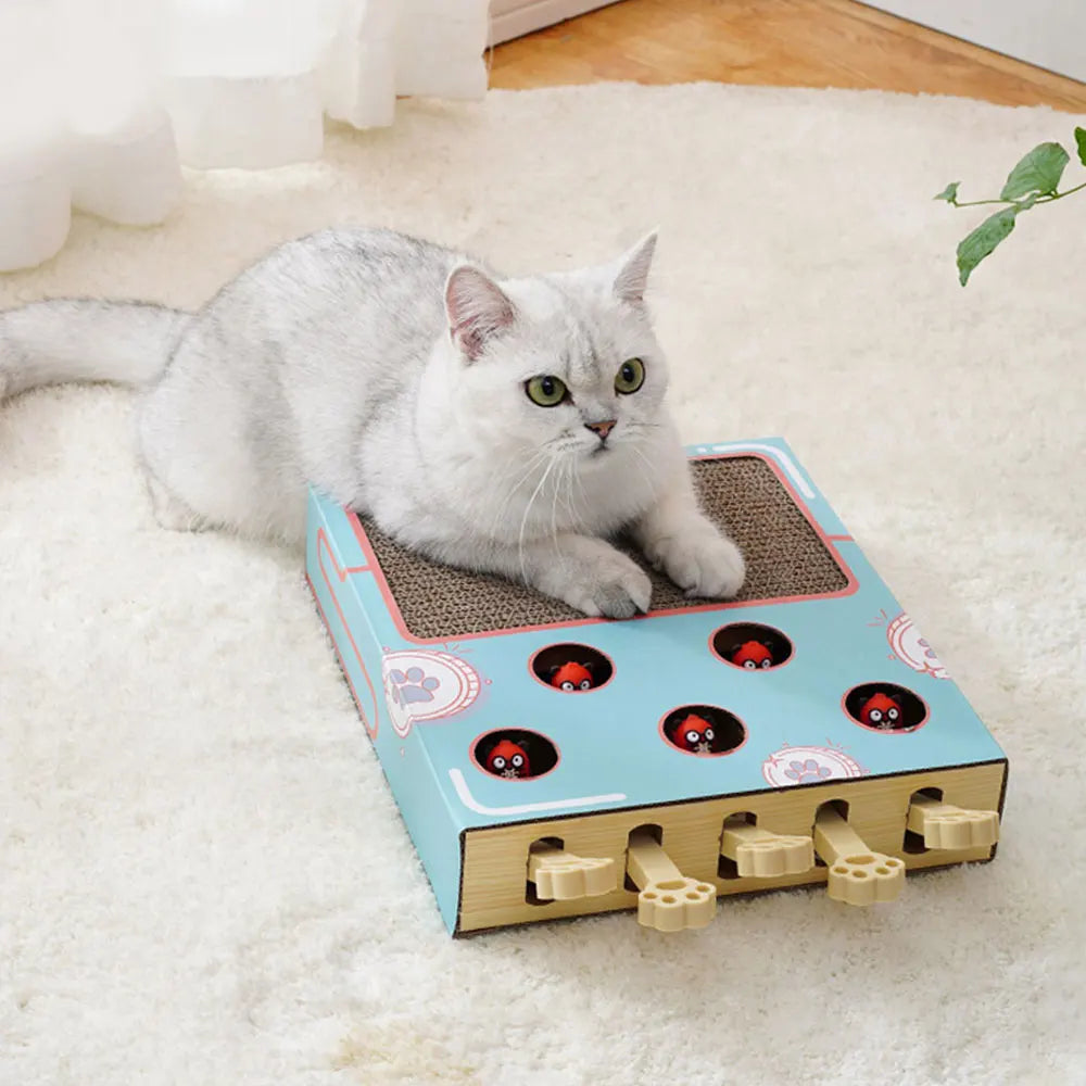 A gray cat is resting on an interactive whack-a-mole style scratching board with holes, lying on a white fluffy rug.