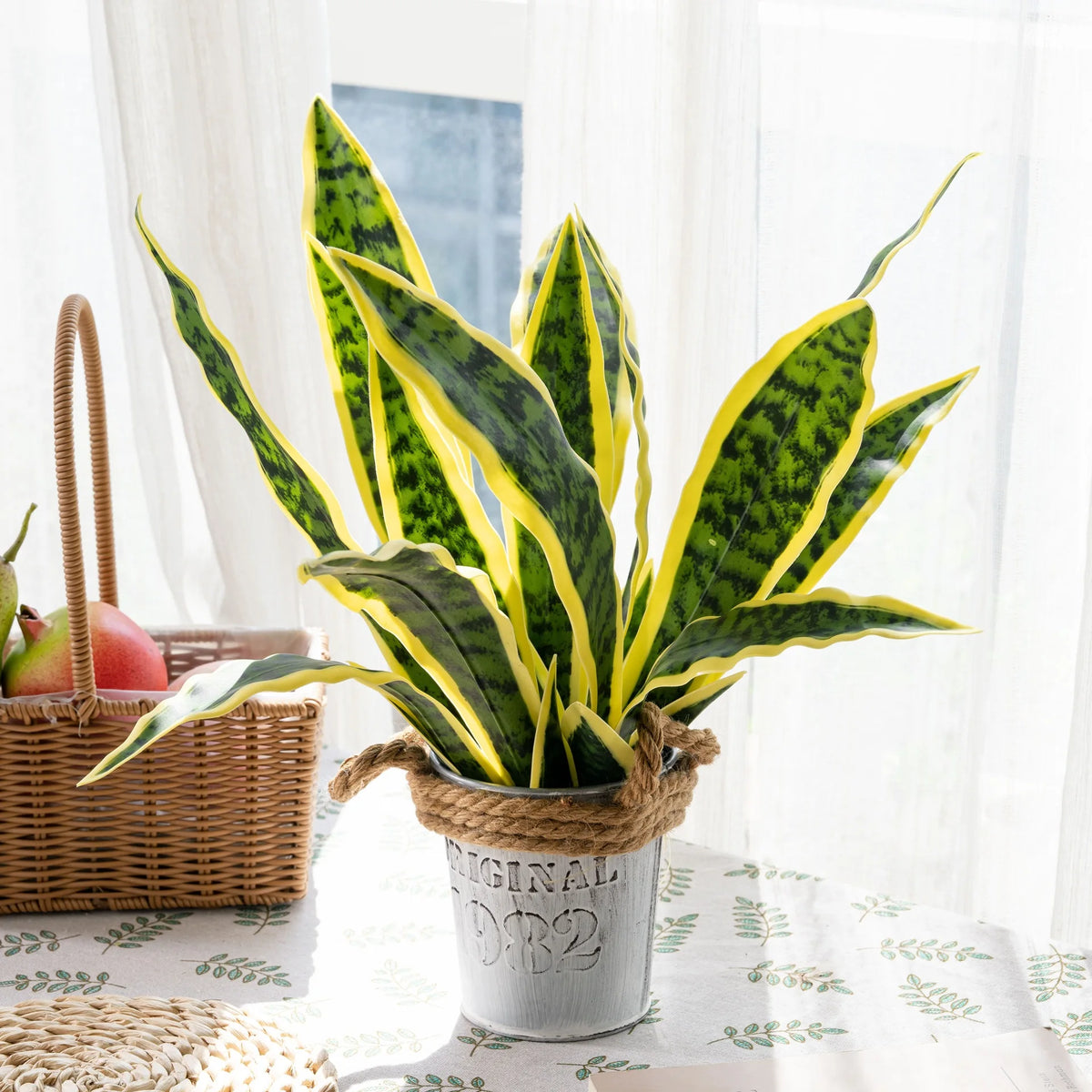 Artificial snake plant with long green leaves in a silver pot on a white table.
