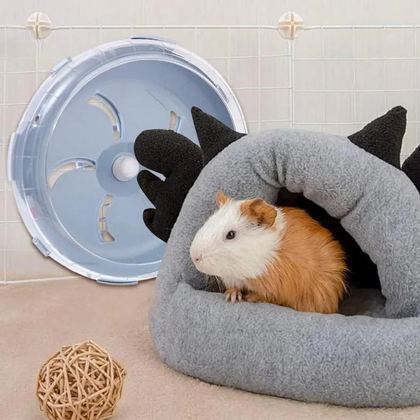 A white and orange guinea pig is resting inside a gray, arched exercise wheel for small pets.