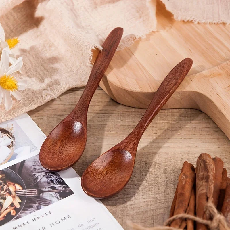 A set of six dark brown wooden tea and coffee spoons resting on a light wooden board with natural fabric.