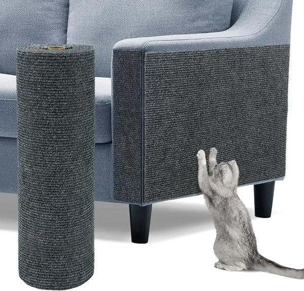 A gray cylindrical cat scratch pad is shown next to a grey upholstered sofa with a cat sitting on the floor.