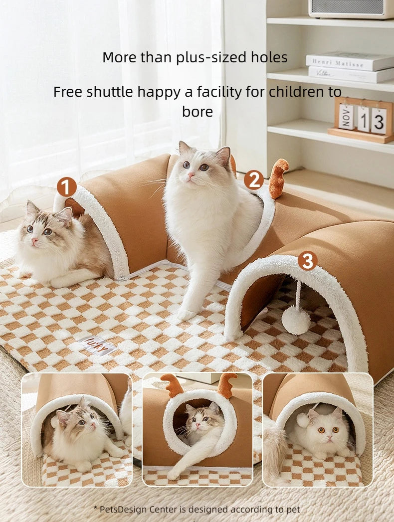 A fluffy white cat is relaxing inside a brown plush bed with an arched reindeer tunnel entrance.