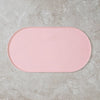 A pink, oval non-slip waterproof feeding mat resting on a light gray concrete surface.