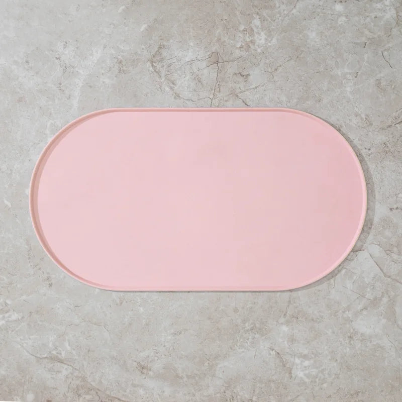 A pink, oval non-slip waterproof feeding mat resting on a light gray concrete surface.
