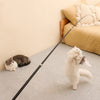 A fluffy white cat is playing with an extended telescopic wand toy on a light gray carpet.