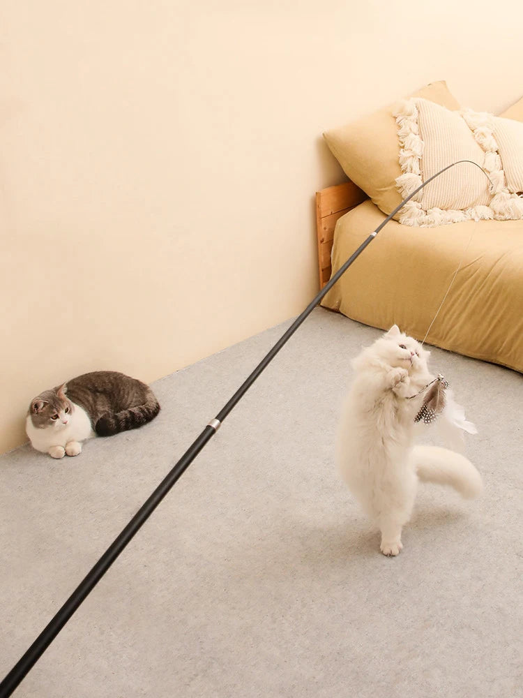 A fluffy white cat is playing with an extended telescopic wand toy on a light gray carpet.