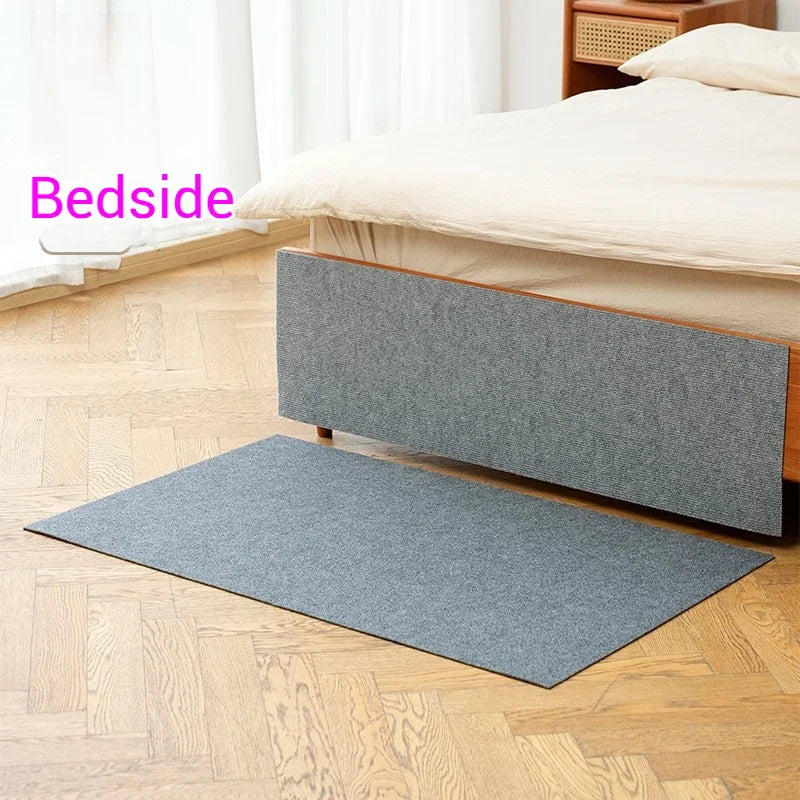 A gray self-adhesive cat scratching mat placed on a wooden floor next to a bed.