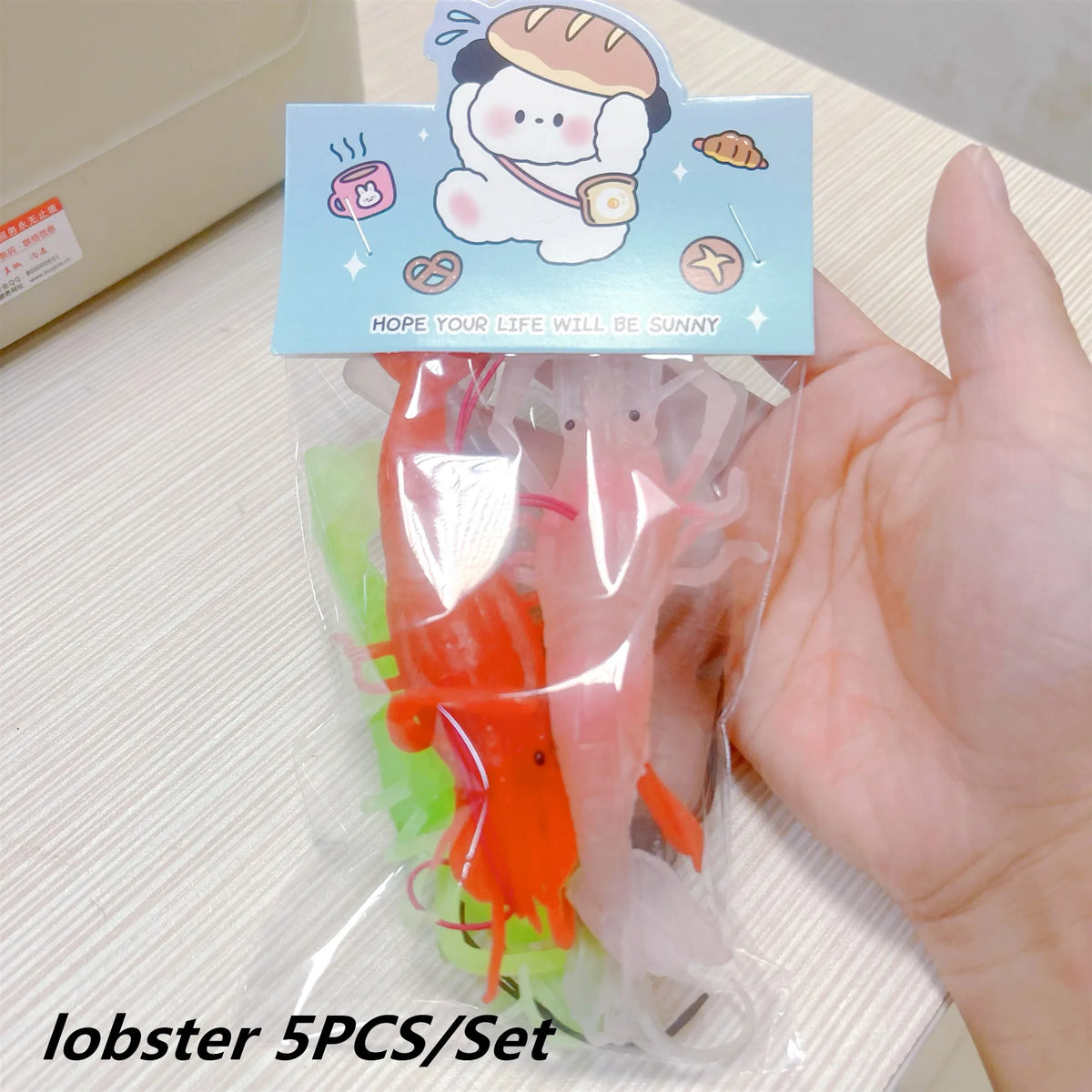 A clear plastic bag contains five rubber lobster bath toys with a cheerful illustration on the top card.