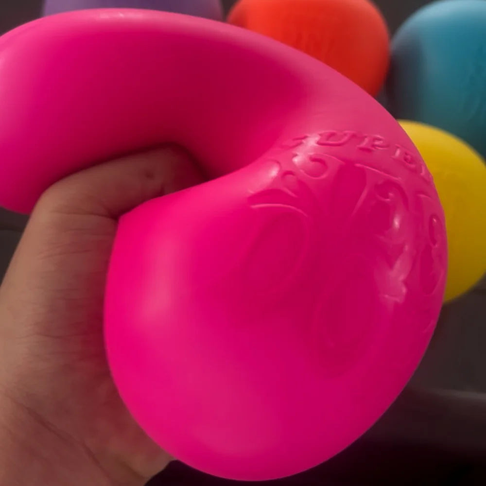 A hand is holding a bright pink, squishy stress ball toy.