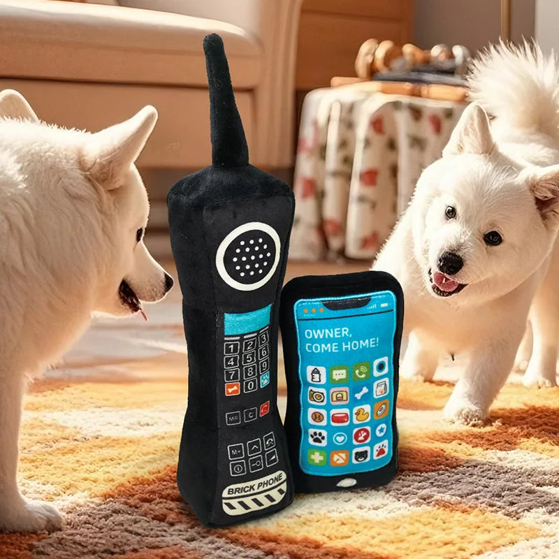 A black phone-shaped squeaky dog toy is placed on a rug next to a fluffy white dog.