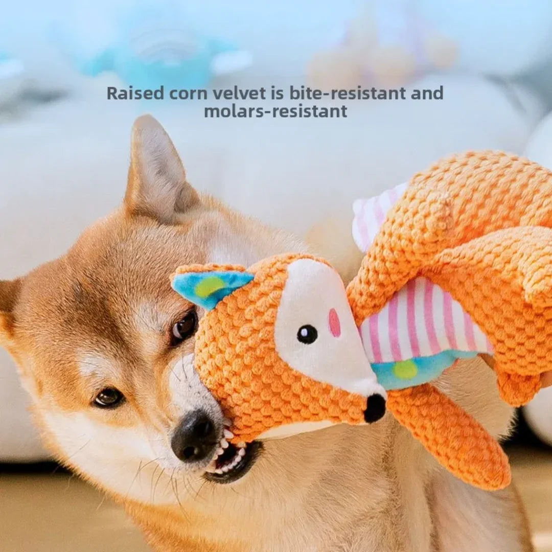 A fluffy dog is holding an orange plush toy shaped like a fox, elephant, and puppy face.