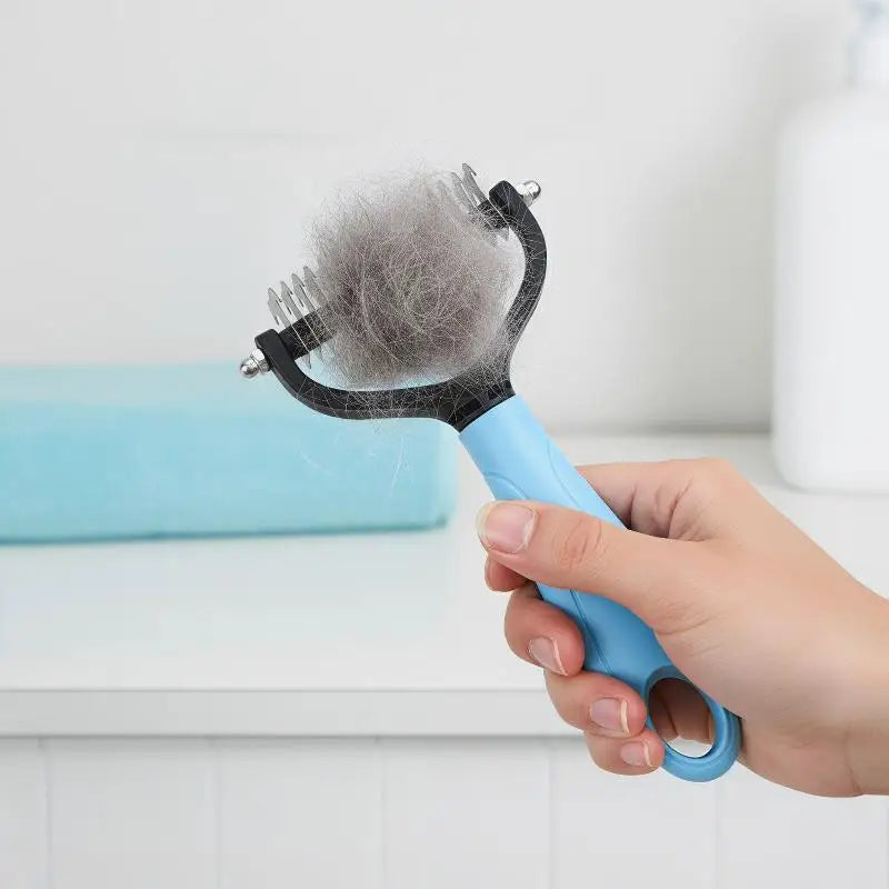 A hand holds a blue pet dematting and deshedding brush with a bristled head against a white background.