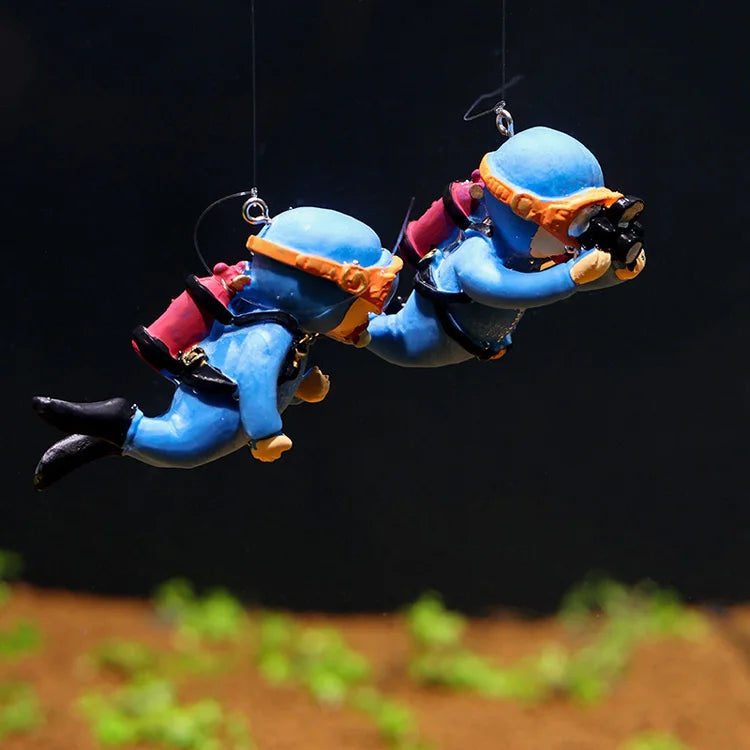 A miniature diver figurine in blue and orange is suspended, appearing to float above a patch of green plants.