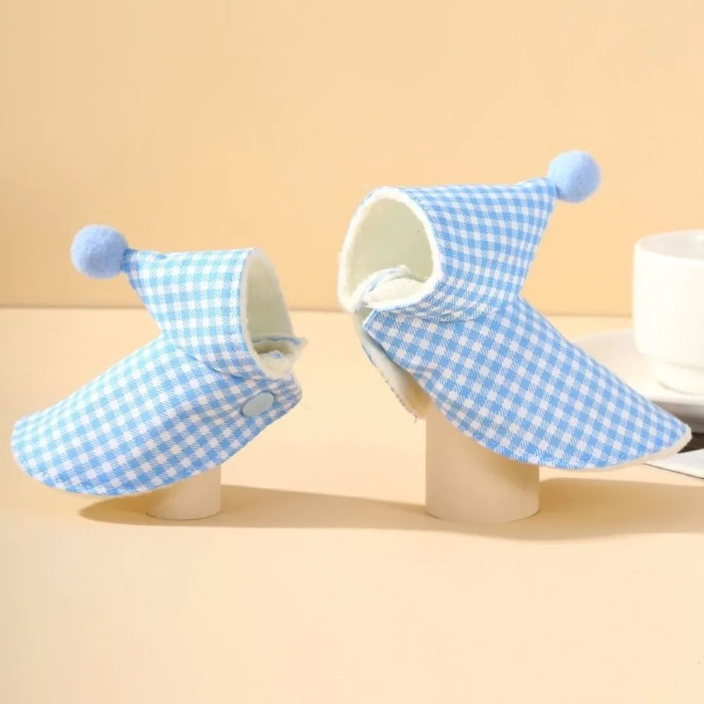 A light blue and white plaid parrot cape and hat set with pom-pom ears displayed on a stand.