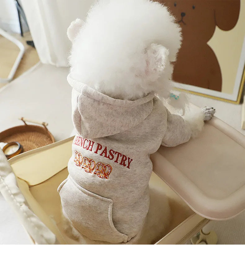 A fluffy white dog wearing a light gray hoodie embroidered with the text FRENCH PASTRY.