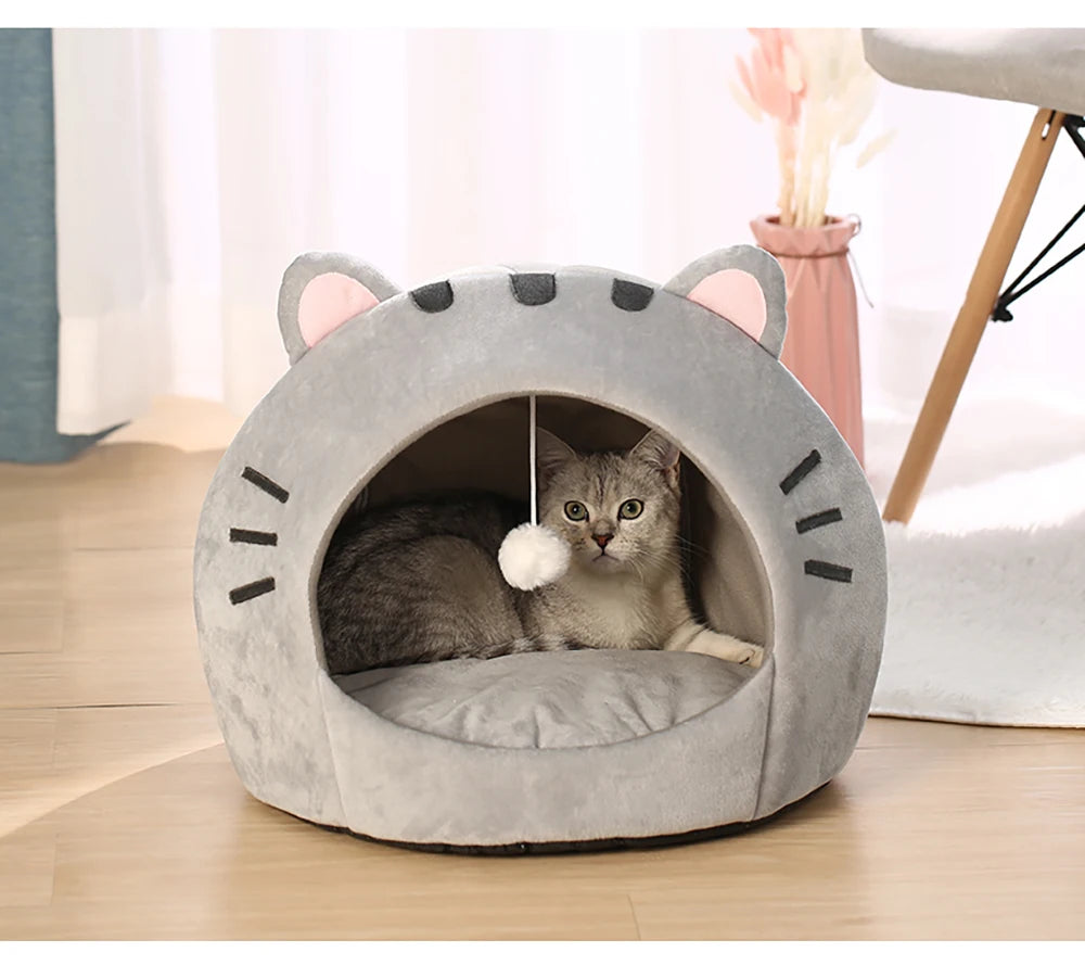 Lit de grotte gris pour chat avec ouvertures d'oreille et coussin, montrant un petit chaton tabby à l'intérieur.