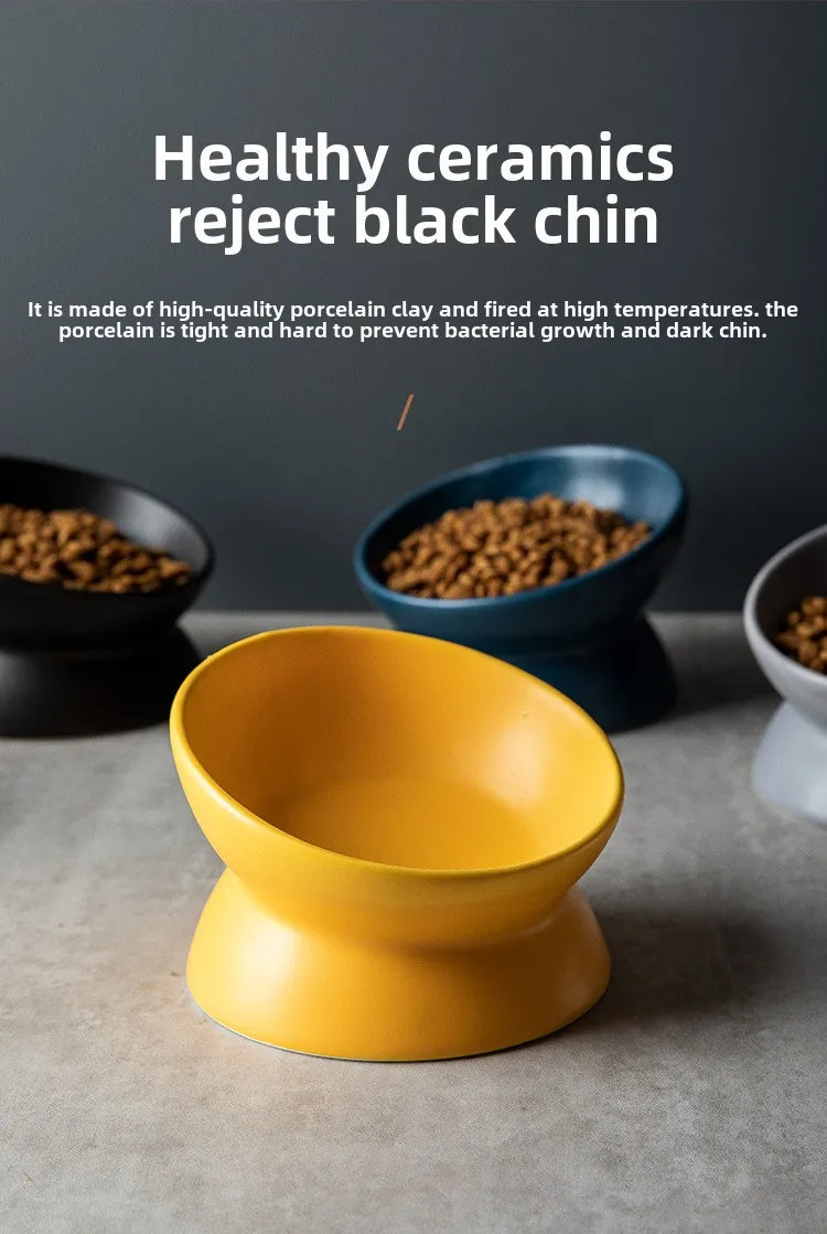 A bright yellow ceramic cat bowl with a raised stand is shown on a gray surface.